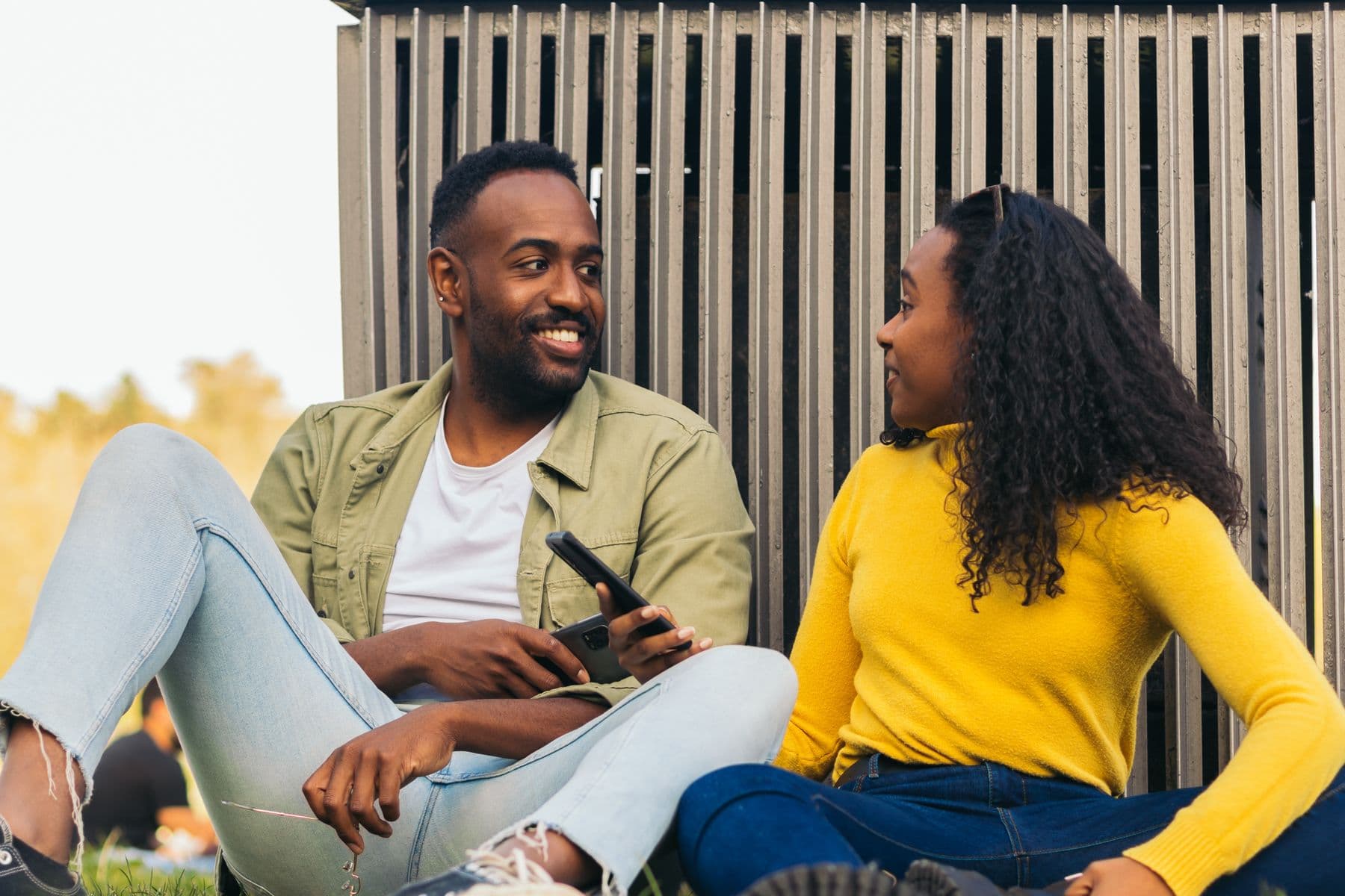 A couple sitting outdoors in warm daylight, talking and smiling