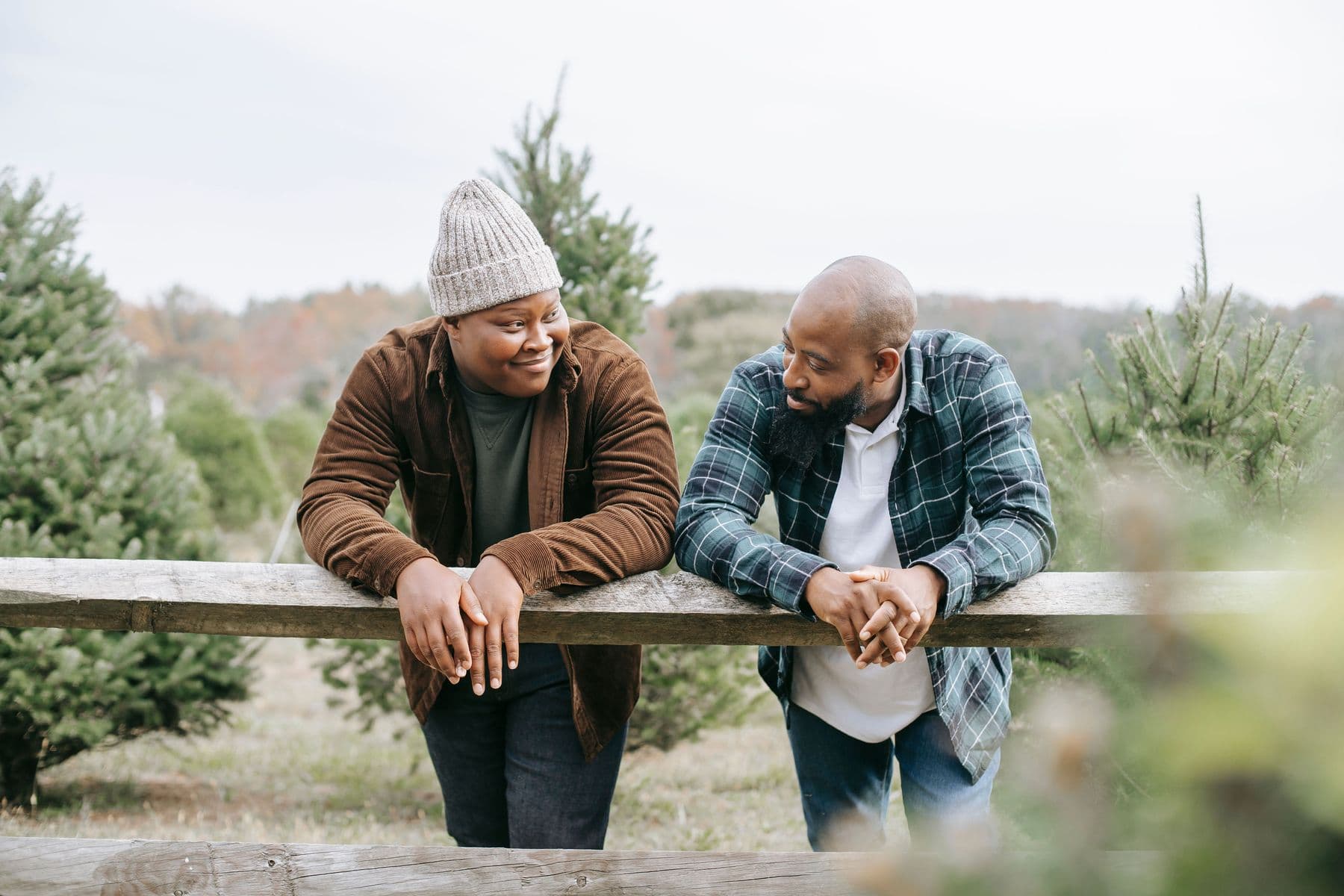 A father and son leaning on a wooden fence among evergreen trees, talking