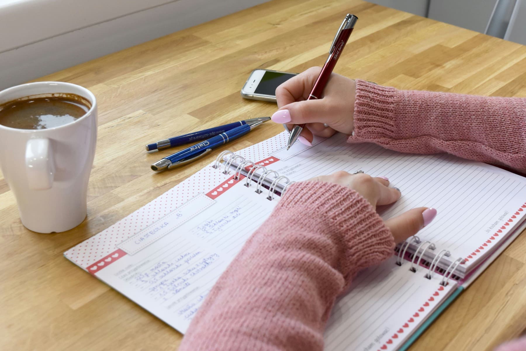 Hands writing in a notebook next to a coffee