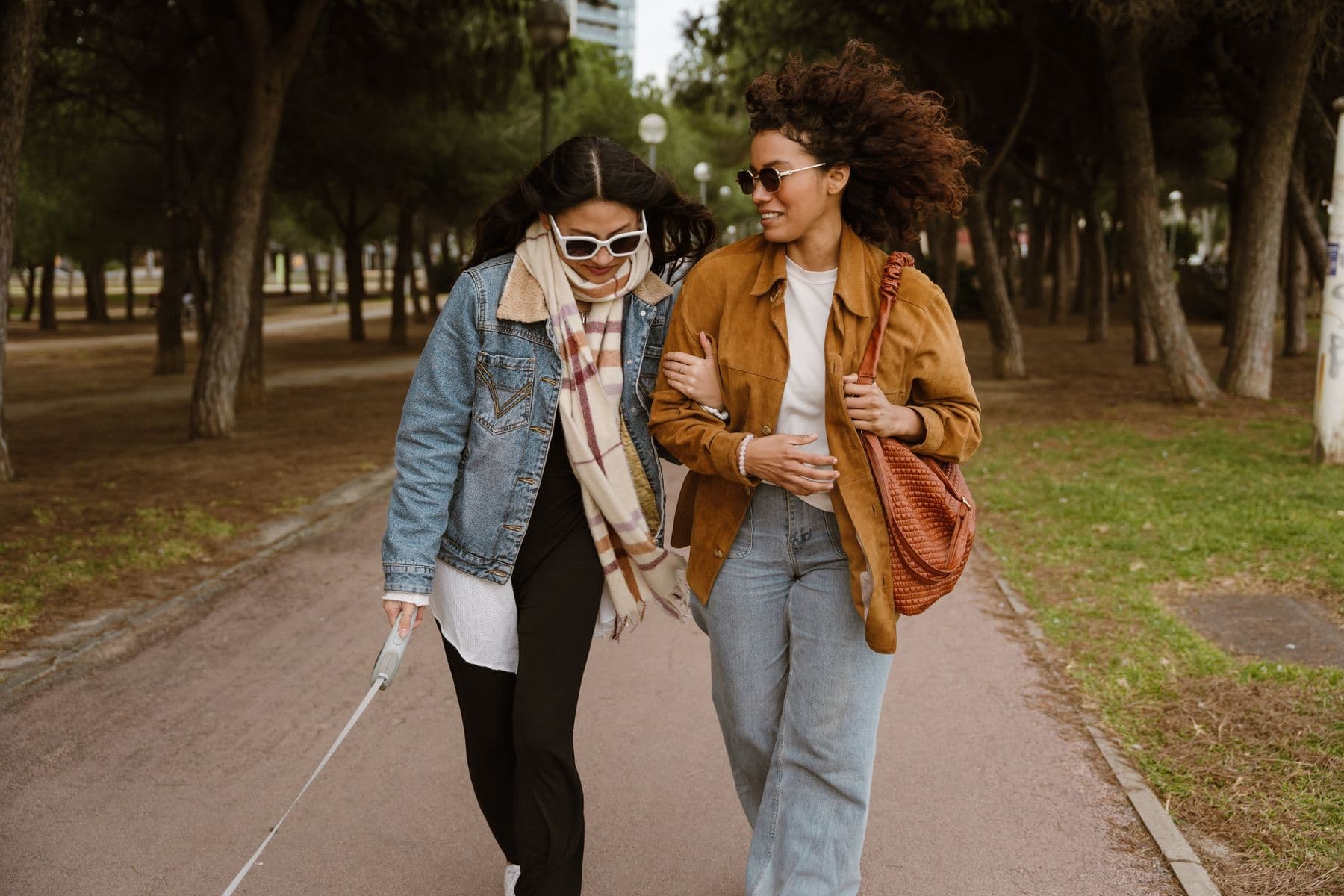Two women walking arm in arm on a tree-lined path